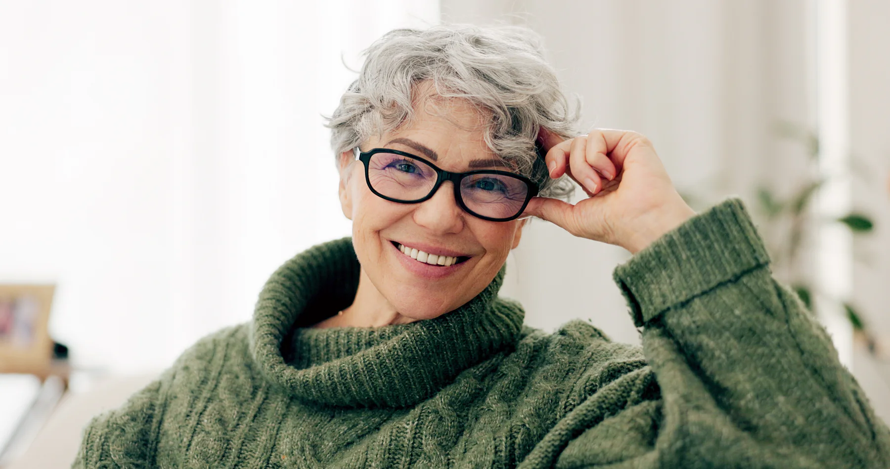 An older woman smiling while putting on her glasses