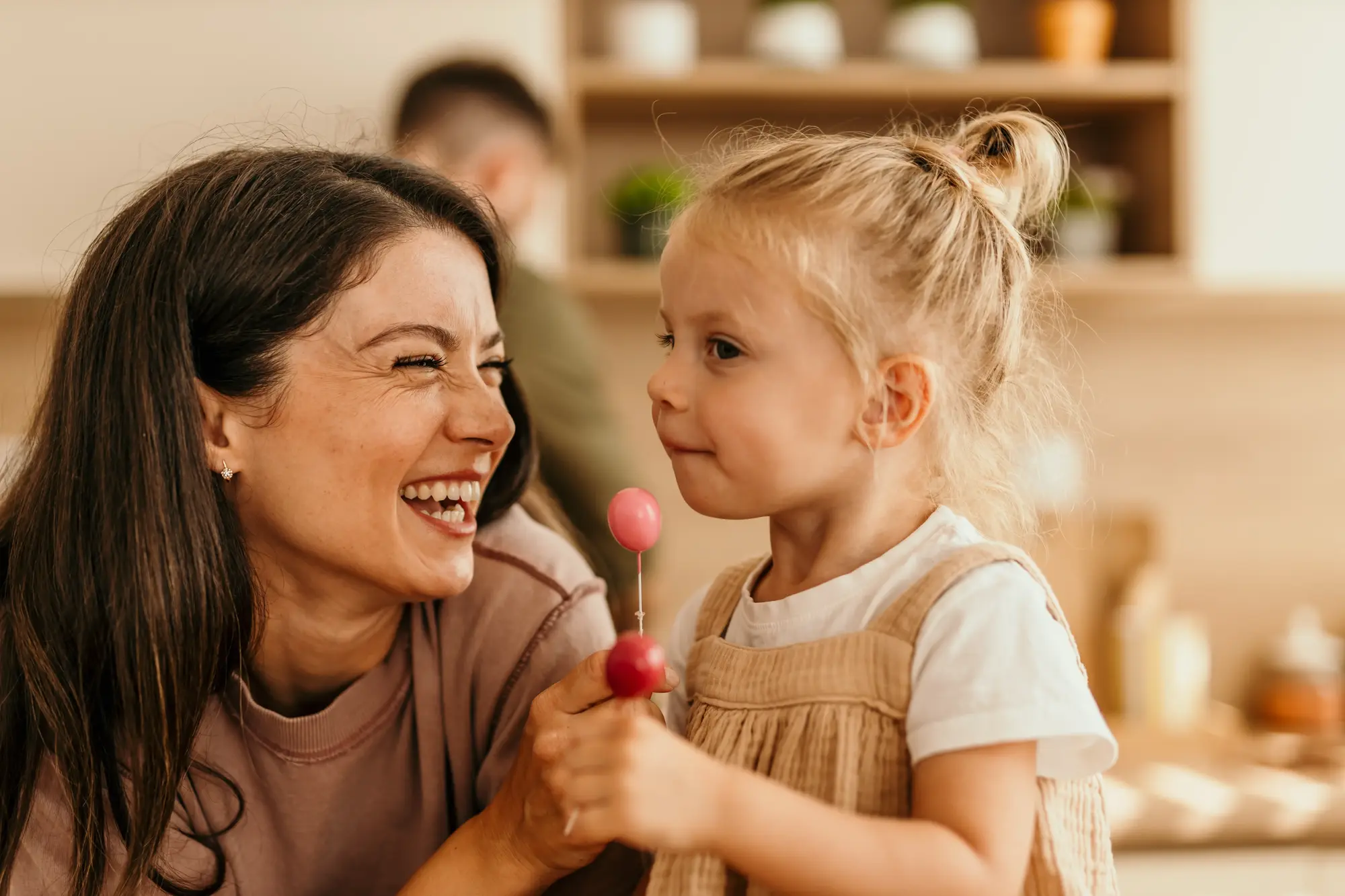 A mother and young daughter laughing together in the kitchen